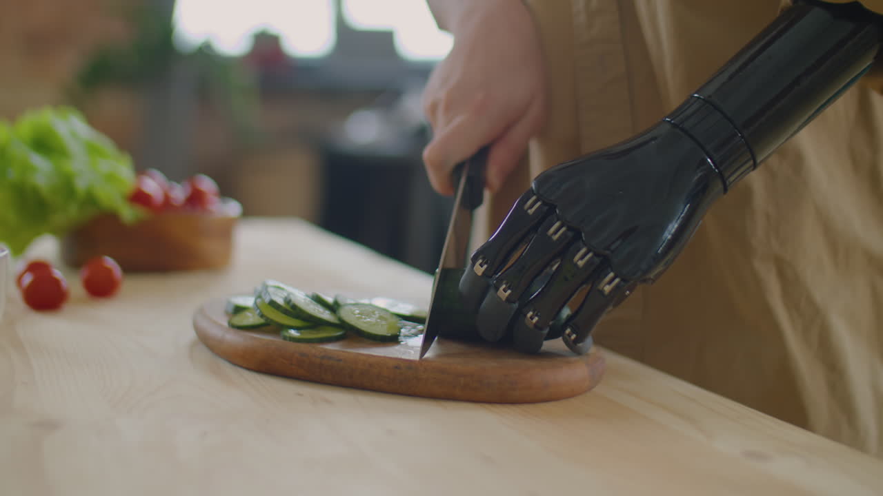 Woman with Prosthetic Arm Cutting Fresh Cucumber at Kitchen Table