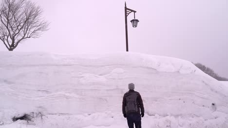 male tourist walking up to very high snow wall in aomori, japan
