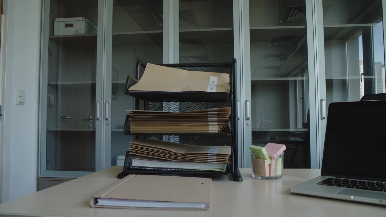 Moving camera focusing on 3-tier letter tray holding manila folders on office desk