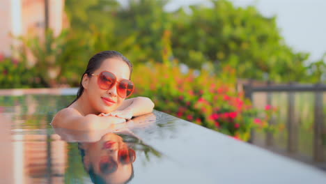 stunning asian female relaxing at border of infinity pool smiling and looking at camera