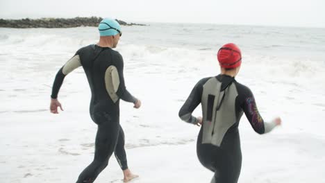 athletic man and woman running on beach with wetsuits