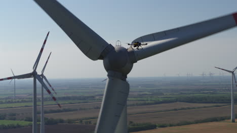 a drone in the air surveying a working wind turbine to the backdrop of a wind farm on flat farm land