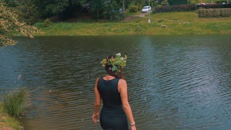 a pretty young happy girl, wearing black dress, entering the pond during outdoor hike in the forest, woman in nature