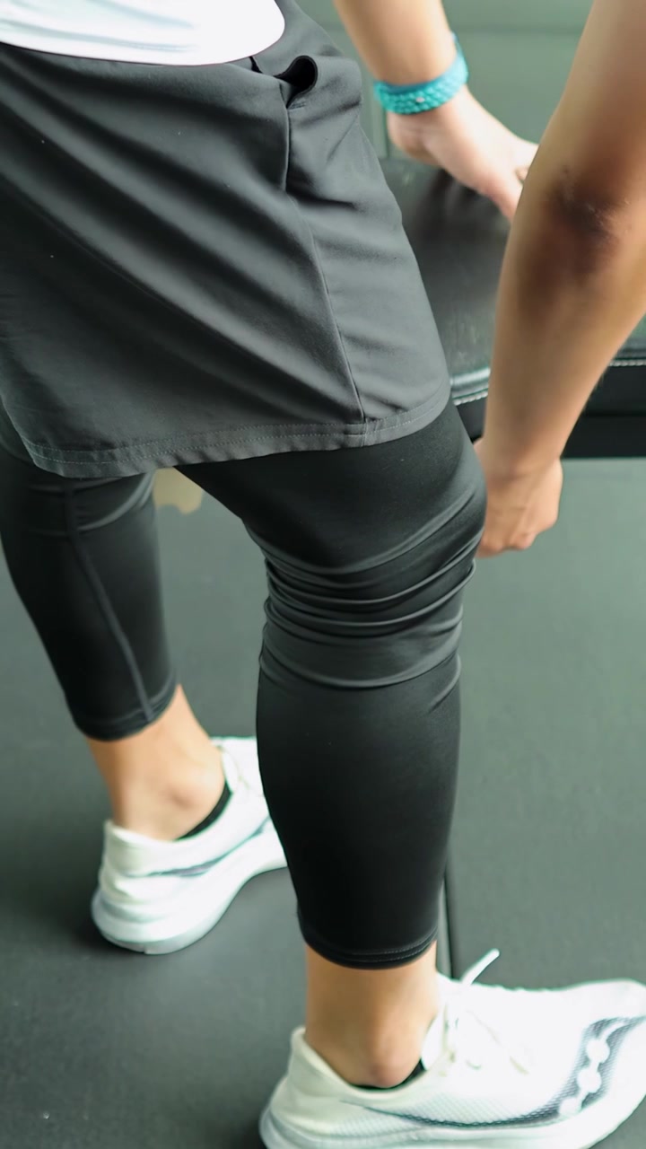 Atleta con ropa deportiva se prepara junto a un banco plano en un gimnasio moderno con iluminación brillante y uniforme.