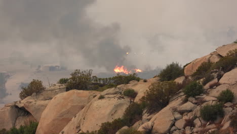 wildfire on top of cliff, bright orange flames, black smoke rises