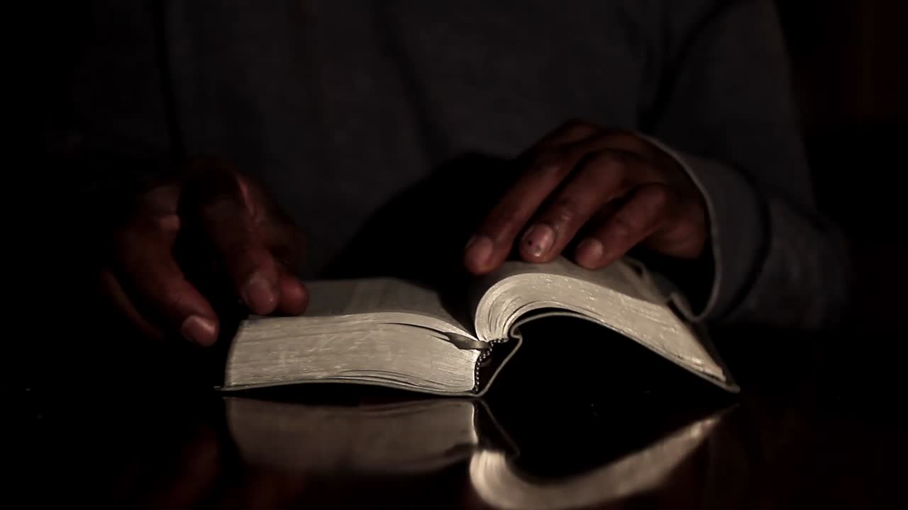 Homme caribéen priant Dieu, les mains jointes, avec une bible et une croix, sur fond noir. Vidéo de stock