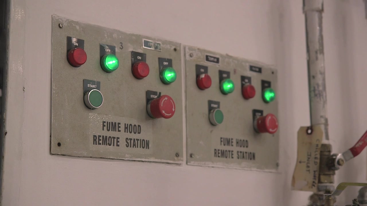 Pannello di controllo della stazione remota della cappa aspirante all'interno di un laboratorio, con interruttori illuminati e pulsanti di arresto di emergenza su un'unità a parete