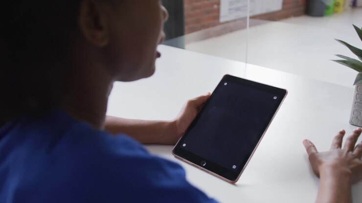Donna d'affari afroamericana seduta a una scrivania in videochiamata utilizzando un tablet, con spazio per la copia