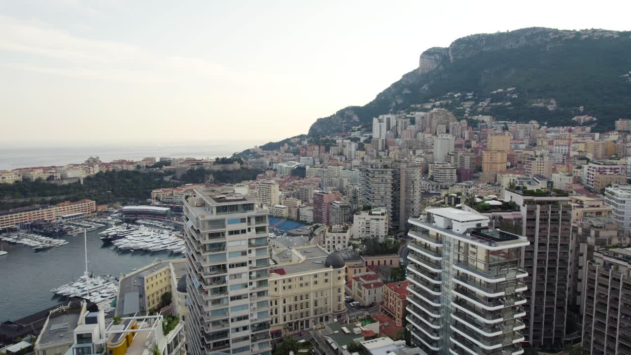 모나코 시내 의 고층 초고층 건물 들, 항구 에 있는 요트 와 배 를 보여 주는 공중 사진
