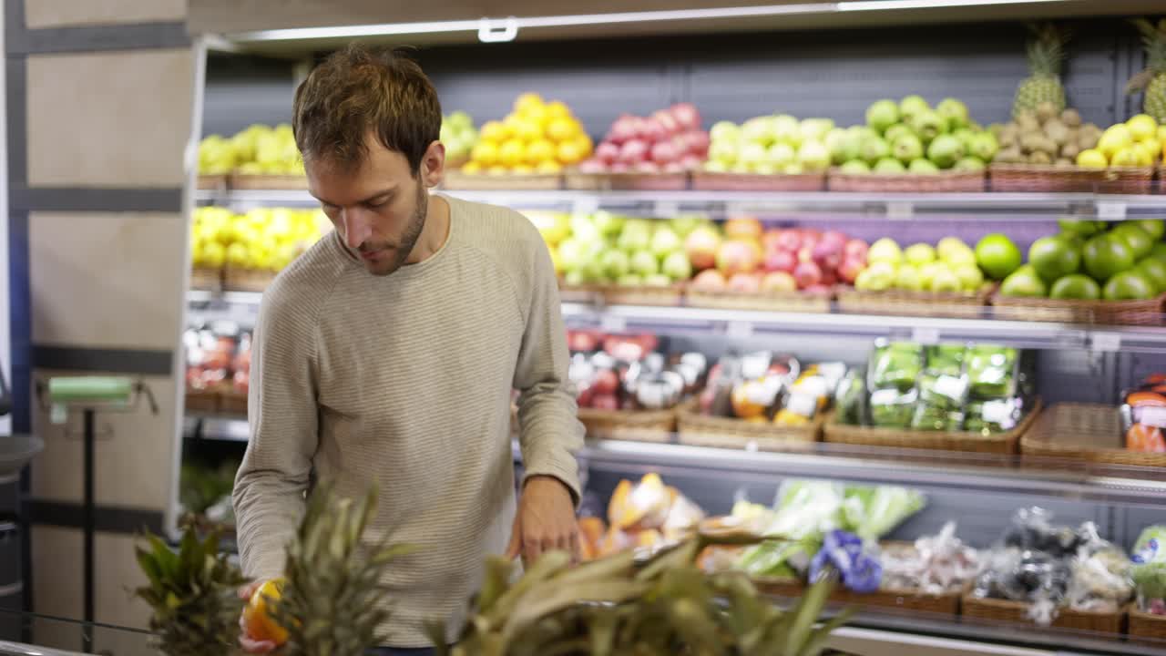 el hombre toma una fruta fresca del estante de alimentos. el comprador elige el caqui en la tienda de comestibles.