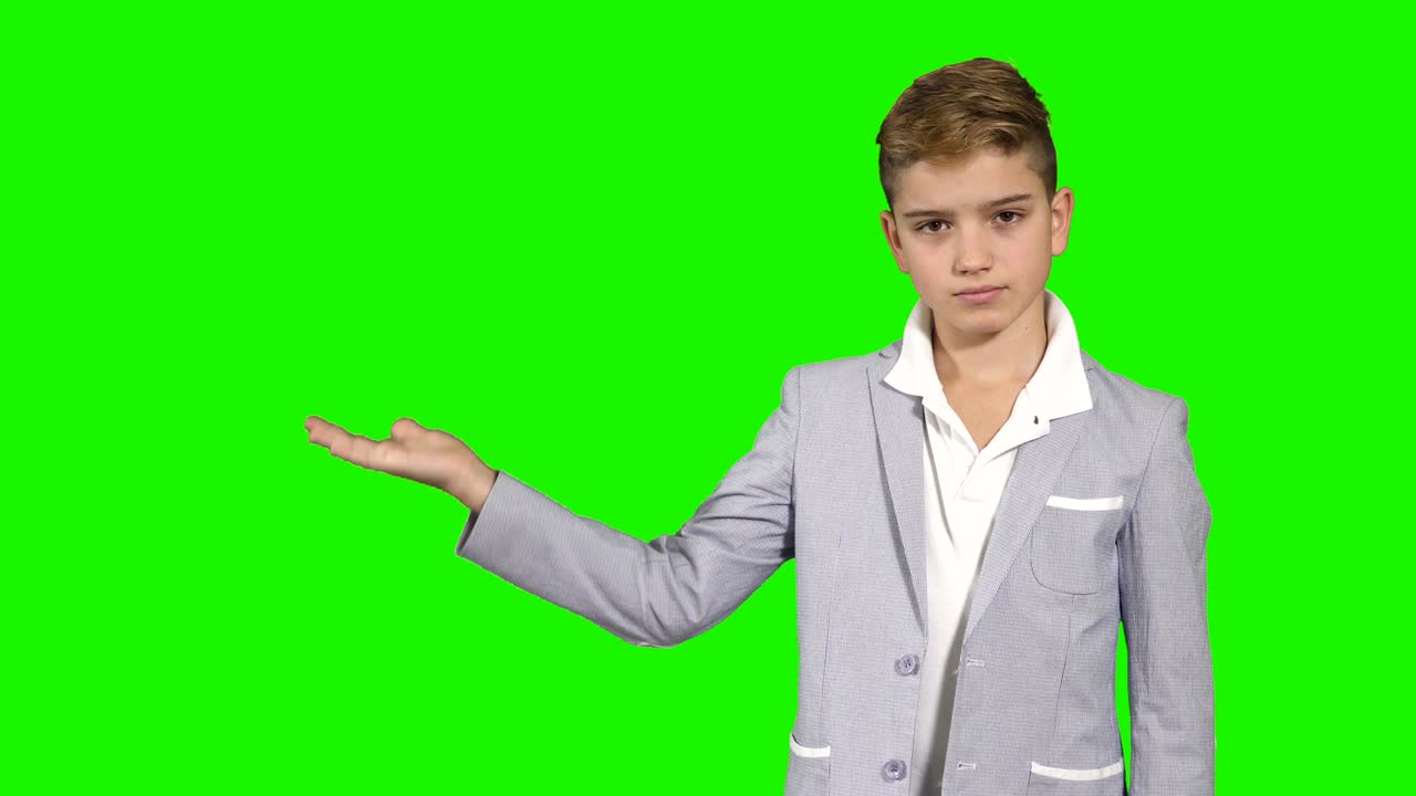 Boy in suit demonstrates something on palm and throw it at green background