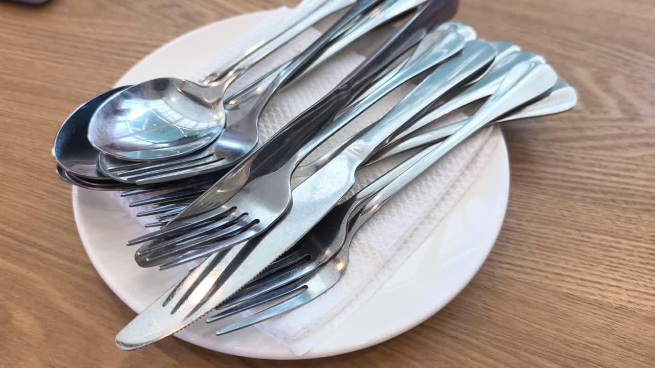 Posate pulite sono disposte ordinatamente su un piatto bianco e un tovagliolo. Le posate sono apparecchiate su un tavolo da pranzo. Tutto è pronto per il servizio del pasto.