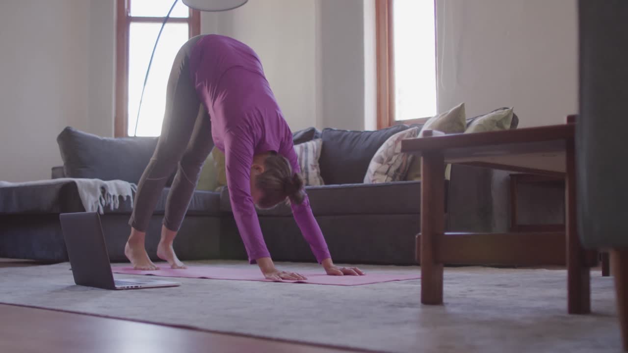 mujer realizando yoga mientras mira la computadora portátil en casa