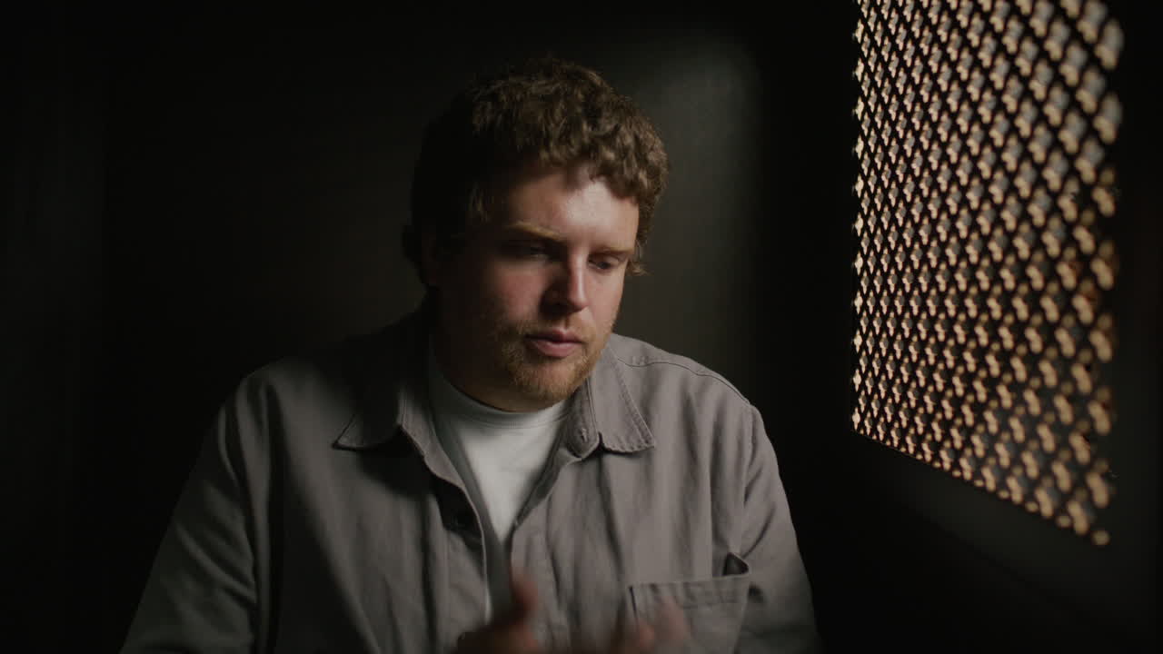 Regretful Young Man Making Confession inside Dimly Lit Booth