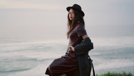 Modelo-Posando-En-El-Crepúsculo-De-La-Naturaleza-Con-Un-Sombrero-Elegante.-Mujer-Sentada-En-El-Mar-Tormentoso