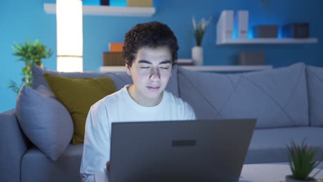 un joven estudiante guapo y divertido enviando mensajes de texto usando una computadora portátil.