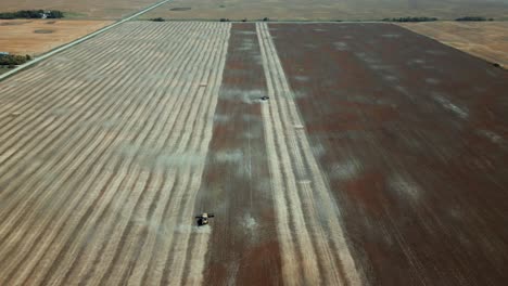 an aerial drone shot of a single farm tractor combine driving harvest lines down a field of wheat