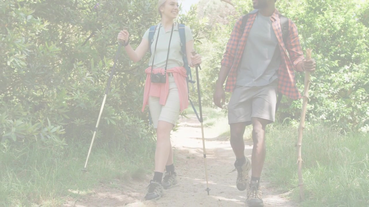 Dos excursionistas entrando al sendero, caminando hacia la cámara, balanceando bastones, pisando raíces por salud.