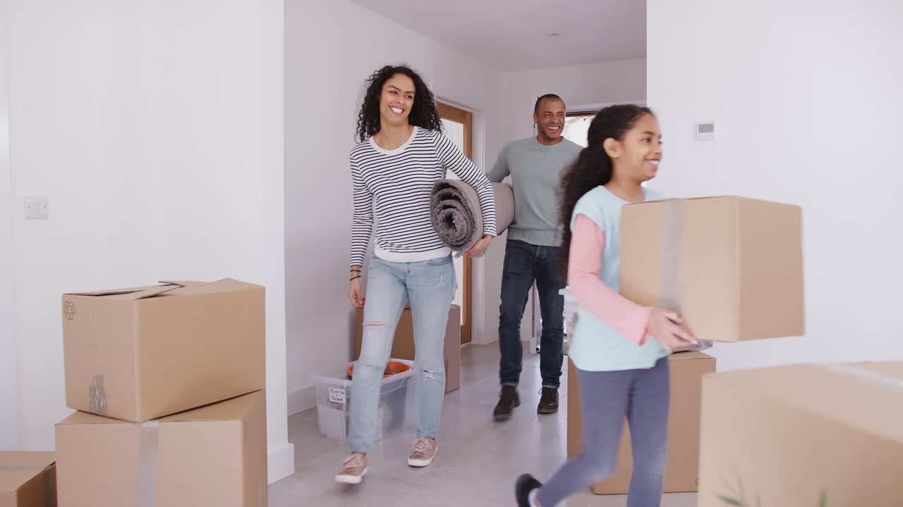 familia sonriente llevando cajas y alfombras a la nueva casa el día de la mudanza