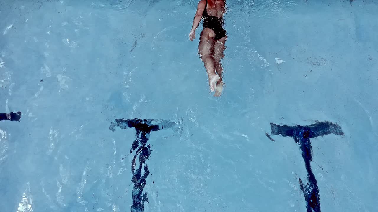 A woman swimming in a pool reaches the end of the lane and turns to complete another lap - overhead slow motion