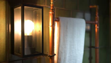 acercamiento de la lámpara de baño artesana anticuada en la pared al lado del carril de toallas rústico en las características interiores de la cabina del campo