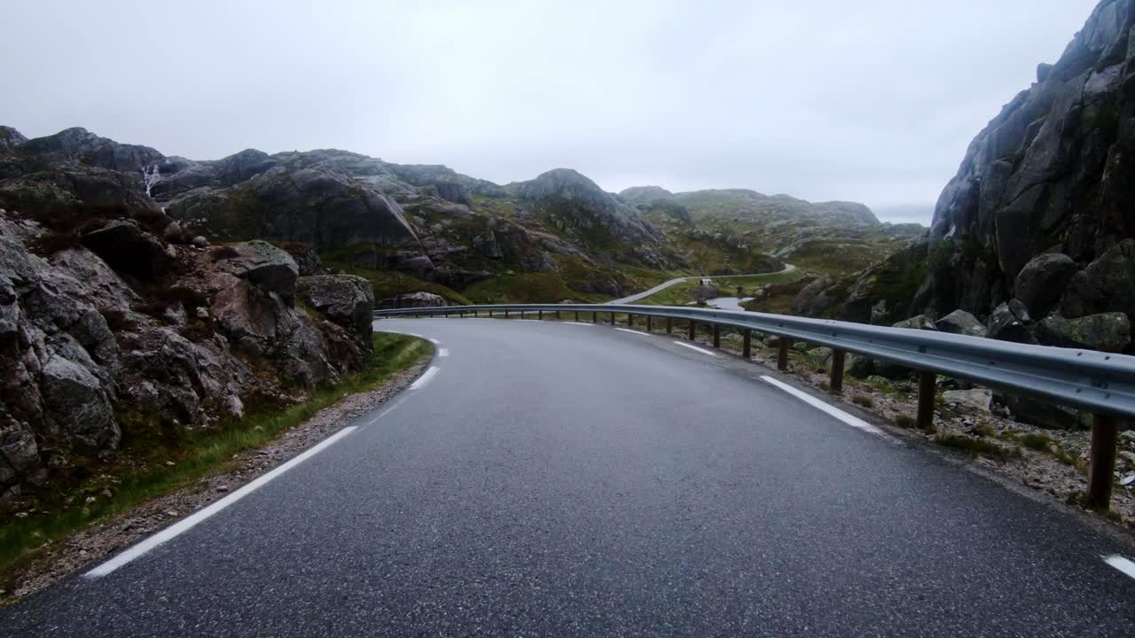 Wet asphalt reflects cloudy sky as a car moves along narrow Norway mountain pass