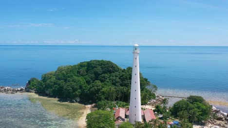 aerial of white lighthouse on remote lengkuas island with tourists in tropical blue water of belitung indonesia