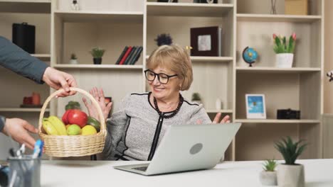 older-woman-presses-a-button-on-her-laptop-and-promptly-receives-a-basket-of-fruits