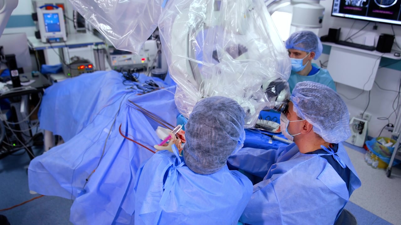 Neurosurgical team performing the surgery using powerful microscope. Male nurse arranges tools at backdrop. Top view.