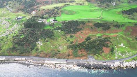 static aerial shot of northern ireland coastal walk near glenarm town with view of a green beautiful landscape, the blue river and idyllic buildings while cars drive on the road