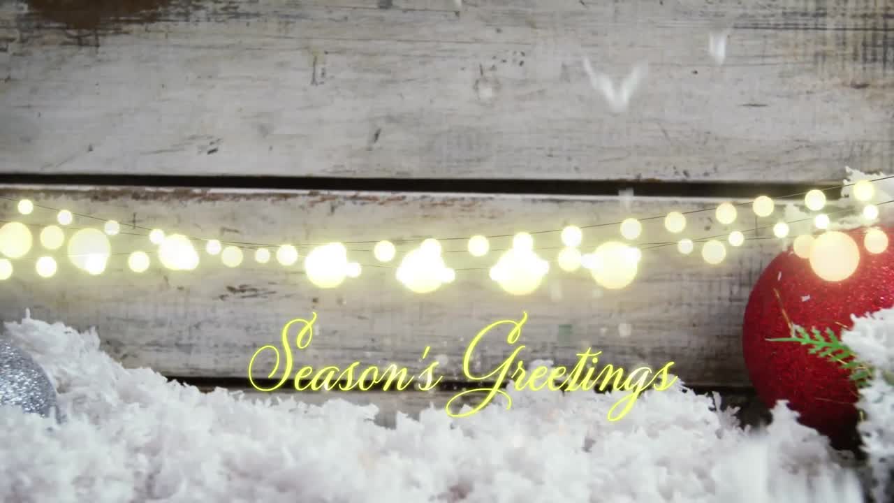 Animation of text, season's greetings, in yellow, over string lights, snow and christmas bauble