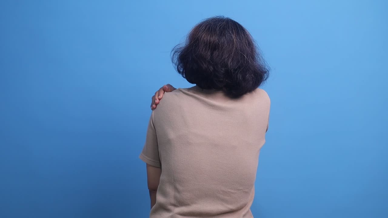 Back view of elderly woman suffering from shoulder pain, hand massaging her shoulder