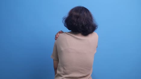 back view of elderly woman suffering from shoulder pain, hand massaging her shoulder