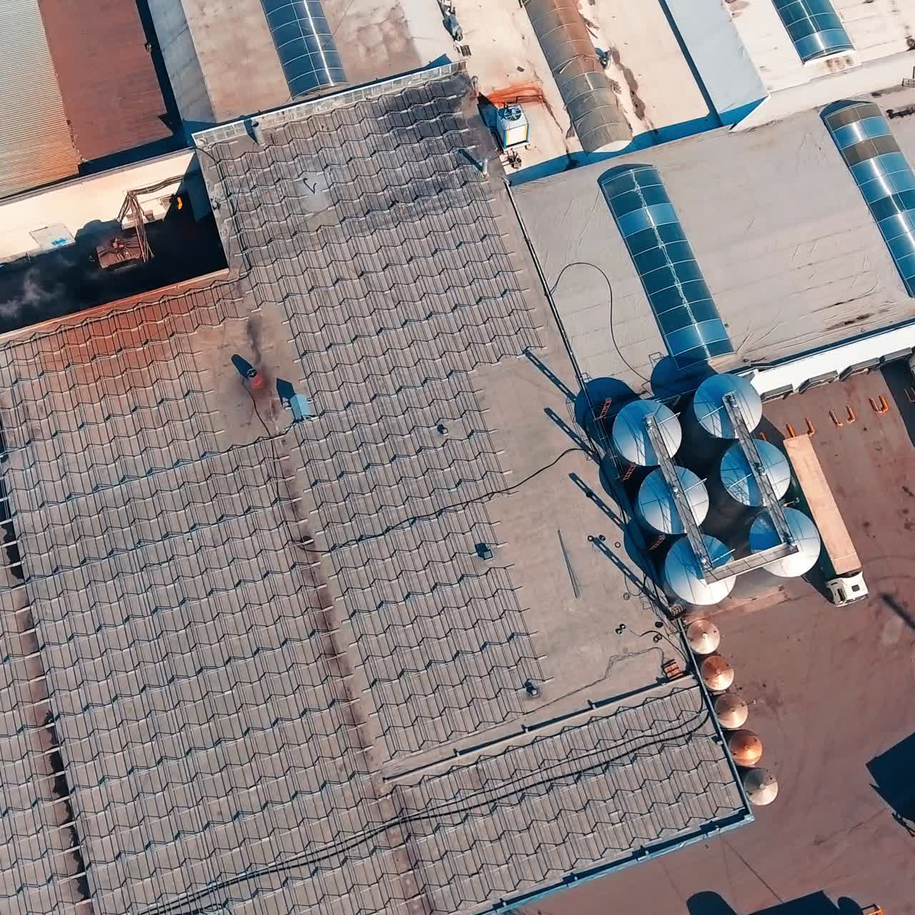 Tops of the warehouses covered with metal constructions. Drone footage rising over the roofs of modern industrial plant. Big lorries waiting for loading at backdrop