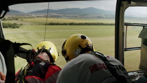 Zwei-Retter-Mit-Gelbem-Helm-Schweben-Im-Rettungshubschrauber-Mit-Offener-Tür