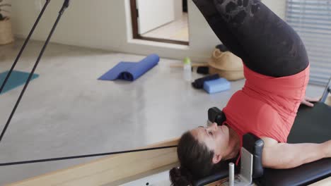 Fit-senior-caucasian-woman-stretching-on-reformer-in-pilates-studio,-unaltered,-in-slow-motion