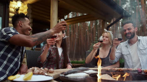 Cheerful-friends-clinking-glasses-on-bbq-party-outside.-Guys-drinking-red-wine