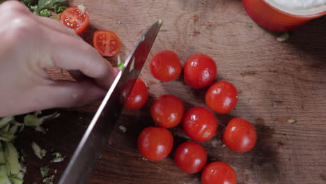 Top-down-view-of-woman-cutting-tomatoes-on-wooden-chopping-board