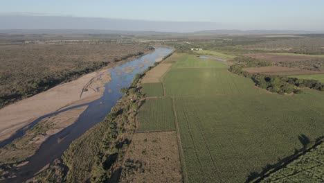 Imágenes-De-Drones-Muestran-Granjas-De-Caña-De-Azúcar-Y-Pimientos-Contrastantes,-Divididas-Por-Un-Río-Estacional,-Que-Bordean-El-Parque-Nacional-Kruger.