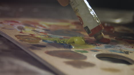 close up someone squeezing a red tube paint on a wooden palette