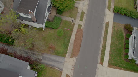 overhead view of houses in suburban neighborhood as drone descends for a landing with the drone pilot in the frame