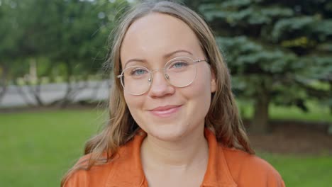 Woman-Headshot-Squinting-Eyes-and-Smiling-in-a-City-Park-with-Orange-Clothing