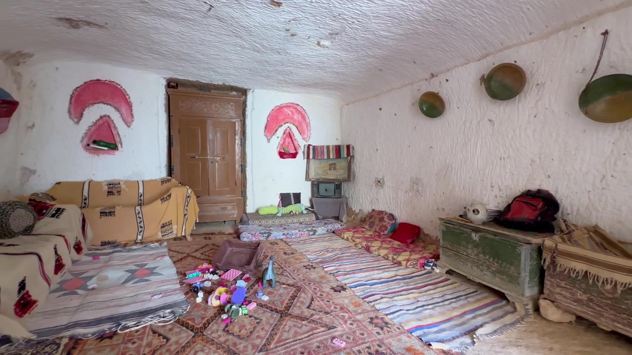 Soggiorno tradizionale in casa grotta di Matmata con tappeti a motivi geometrici, sedute basse e tessuti berberi fatti a mano in un semplice interno sotterraneo, Tunisia