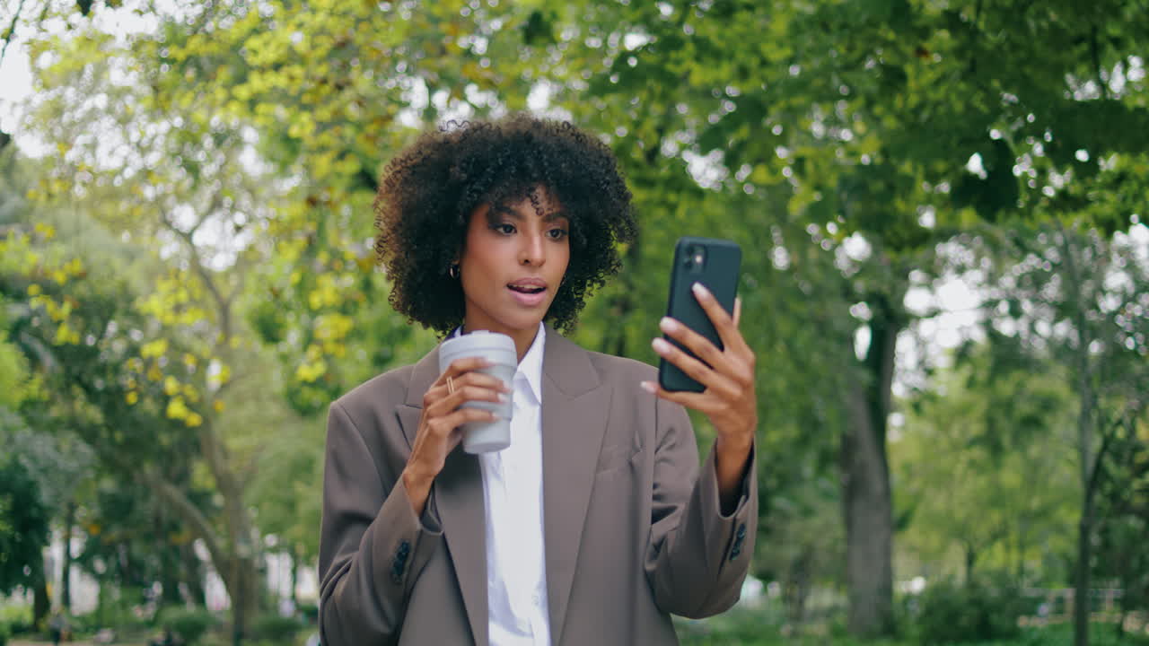 Donna sicura di sé che parla alla telecamera mentre cammina nel parco con un caffè, primo piano. Ragazza che parla.