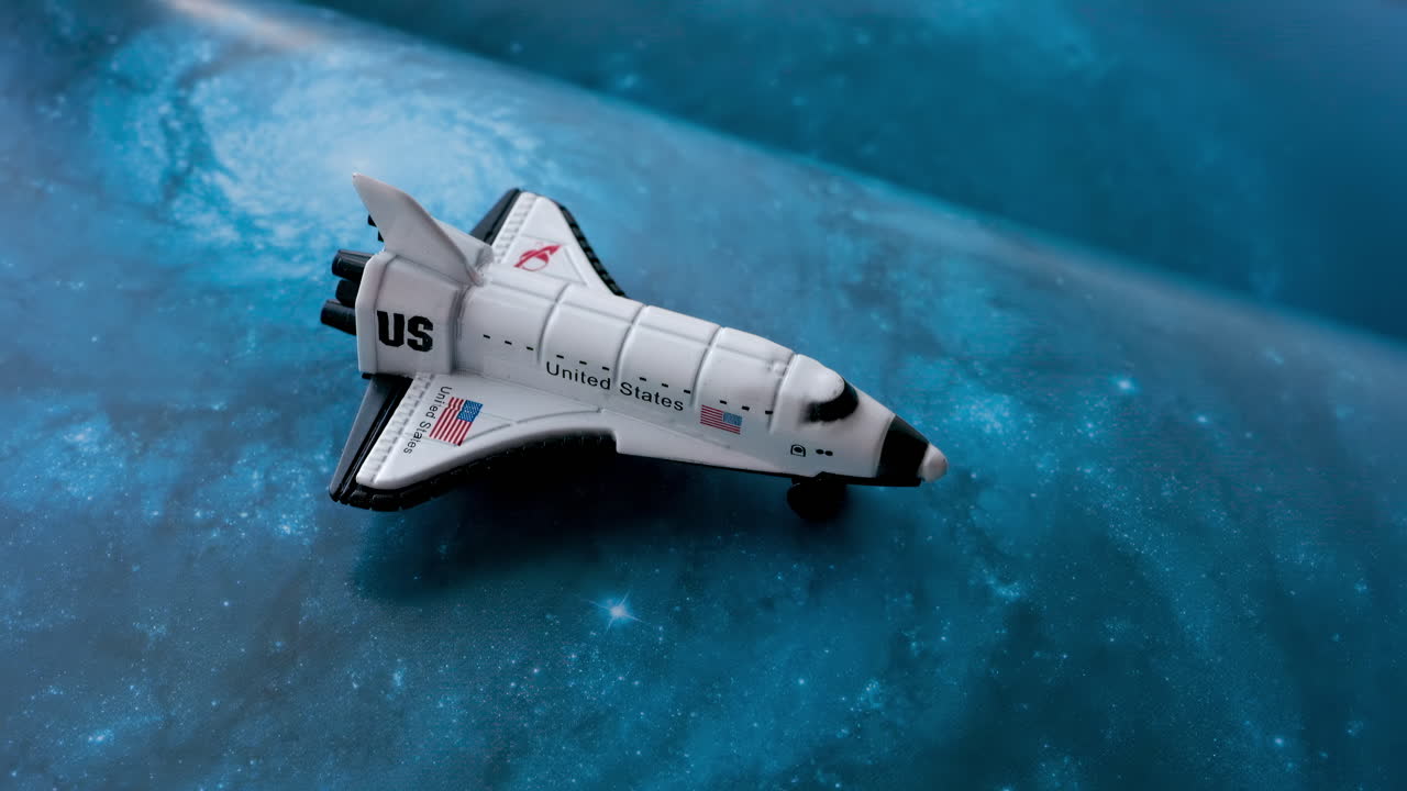 Close up of a miniature toy space shuttle placed on a blue cosmic galaxy backdrop