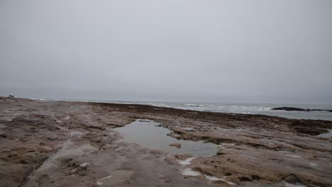 Eine-Pfütze-An-Einem-Felsigen-Strand-Mit-Dem-Meer-Im-Hintergrund-An-Einem-Bewölkten-Tag