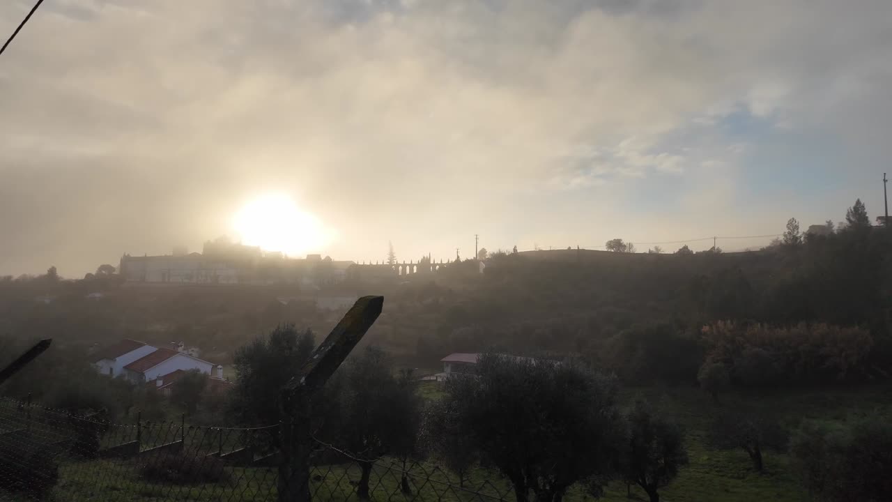 Alba nebbiosa vicino a Tomar, Portogallo. Colline nebbiose e una strada rurale con recinzioni brillano nella morbida luce del mattino mentre il sole sorge dietro il crinale.