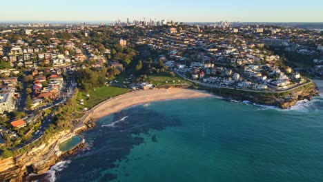 Vista-Aérea-De-La-Playa-De-Bronte,-El-Parque-Y-El-Suburbio-Costero-De-La-Ciudad-De-Bronte---Baños-De-Bronte-Con-Agua-Azul-Clara-Al-Atardecer-En-Nsw,-Australia