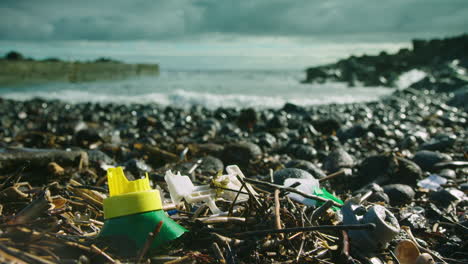 Broken plastic waste lies washed up on a beach, with waves breaking behind
