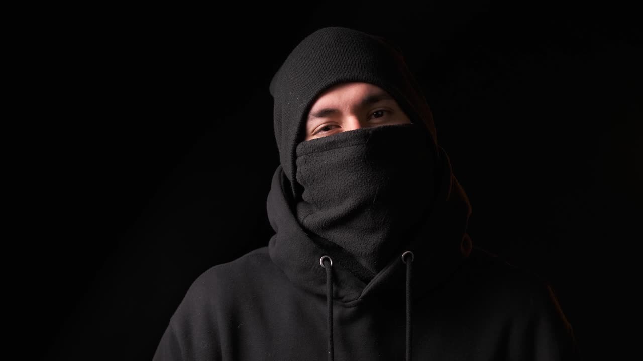 Thief staring at the camera while standing on a dark background.